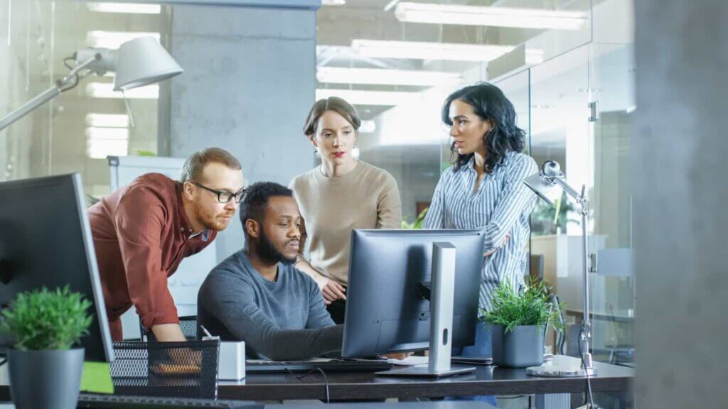 A group of professional men and women work around a computer monitor.
